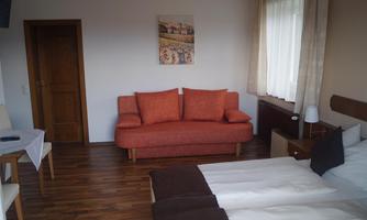 A cozy room with two beds and a red sofa. Plenty of daylight through the windows and a warm wood design.