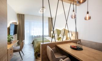 A modern bedroom with wooden decor and a comfortable bed. The room features large windows and an elegant dining table.