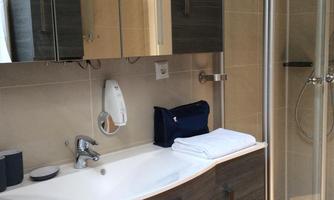 A modern bathroom with a shower and a sink. The walls are light tiled and there is a large mirror cabinet.