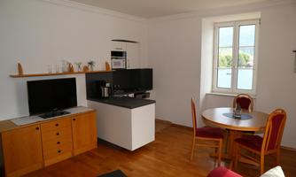 A bright living space with modern furniture. It features a television, a table with chairs, and a window with a view of the landscape.