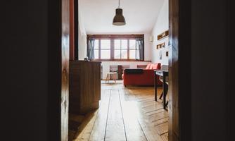 A cozy living room with a red sofa and wood-paneled floors. The light falls beautifully through the window.
