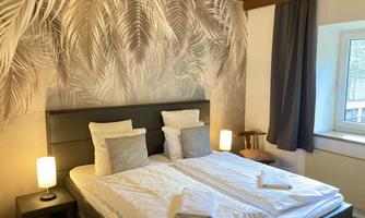 A cozy bedroom with two beds and a stylish wall design of leaves. The soft lighting creates a pleasant atmosphere.