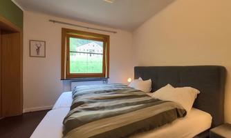 A cozy bedroom with two beds and striped bed covers. A window offers a view of nature.