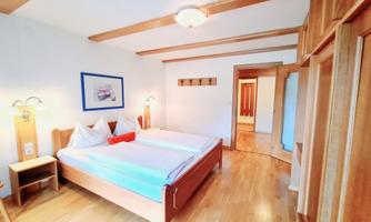 A cozy bedroom with two beds and wooden details. The room has light walls and a modern decor.