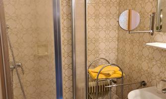 A small bathroom with a shower cabin and a sink. Decorative tiles and a towel holder are visible on the wall.