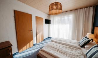 A bright bedroom with a large bed and modern furniture. The windows are dressed with curtains and there are two doors in the room.
