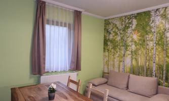 A cozy living space with a green wall paint and a wooden table. A natural pattern with trees can be seen on the wall.
