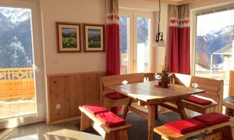 A cozy dining area with a wooden bench and a large table. Through large windows, you have a beautiful view of the mountains.