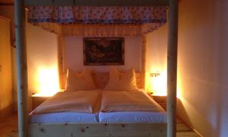 A cozy bedroom with a four-poster bed and soft lighting. The walls are in warm colors, and there is a beautiful picture above the bed.