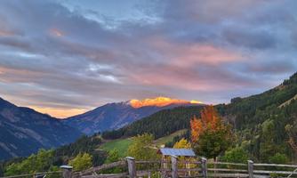 A picturesque mountain landscape with gentle hills and colorful autumn foliage. The mountain peak shines in the sunlight on the horizon.