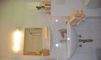 A modern bathroom with a sink, a mirror, and plants on a shelf. Yellow and white towels and toiletries are neatly arranged.