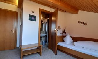 A cozy room with a single bed and wooden details. The walls are light and a small table stands next to the bed.