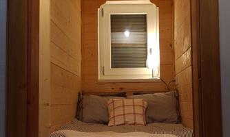 A cozy sleeping area with wood paneling and a window. On the bed are pillows and a blanket, the ambiance is warm and inviting.