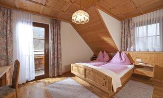 A cozy bedroom with wood paneling. There is a double bed with pink pillows and a table with chairs.