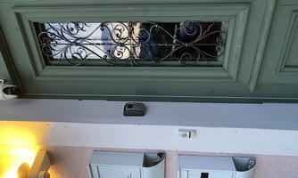 A green front door with an ornate window and a mailbox nearby. A small lamp shines by the door.