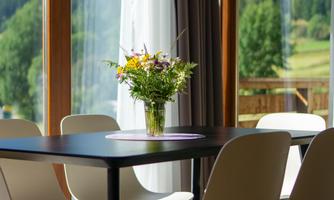 A bright room with large windows overlooking the green hills. On a table stands a vase with fresh flowers.