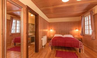 A cozy bedroom with wooden walls and a double bed. The decor is rustic, featuring a red carpet and warm lighting.