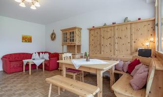 A cozy living space with a wooden table and benches. Red sofas and a wooden cabinet create a warm atmosphere.