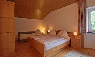 A cozy bedroom with two beds and wooden furniture. It features pleasant lighting and a window view.