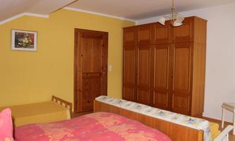 A cozy bedroom with yellow walls and a large wooden wardrobe. There is a bed with colorful bedding and a simple furniture arrangement.