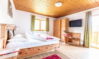 A cozy bedroom with wooden paneling and a large window. There is a double bed, a television, and a small table with chairs.
