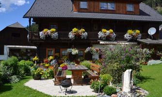 A pretty wooden house with colorful flower boxes. In the foreground, there is an inviting seating area with a garden landscape.