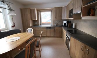 A modern kitchen with wooden furniture and a dining table. The window provides plenty of daylight in the room.
