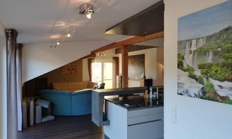 A modern living room with a view of an open kitchen. The décor is bright and inviting, with a large sofa and a painting on the wall.