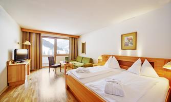 A cozy hotel room with a large bed and a view of the mountains. The decor is modern and bright, with a small sofa and a table.