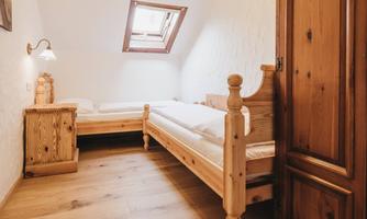 A simple room with two wooden beds and a wardrobe. Light falls through a skylight, creating a bright atmosphere.