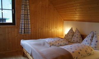 A cozy bedroom with wooden paneling and two beds. A warm atmosphere is created by the soft lighting.