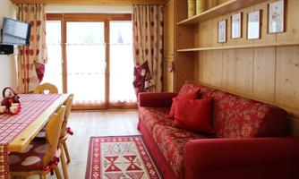 A cozy living room with a red couch and wooden paneling. The room is bright and inviting, with a dining table and large windows.