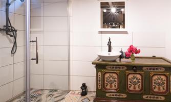 A modern bathroom with a shower cabin and a stylish sink. On one wall stands a decorative chest with a floral arrangement.