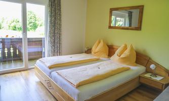 A bright bedroom with two beds and cozy pillows. Large windows provide a view of nature outside.