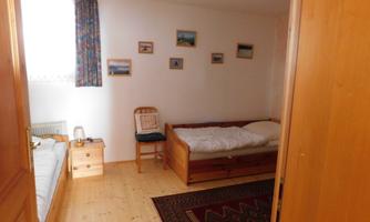 A simple bedroom with two beds and a chair. There are wooden cabinets and pictures on the walls.