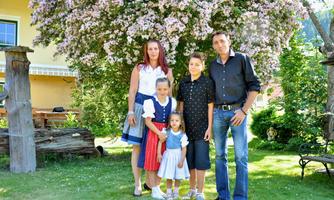 A family stands in the garden under a blooming tree. The children are wearing festive clothing and smiling kindly at the camera.