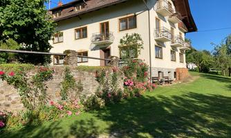 A beautiful residential building with balconies and a well-maintained garden. Colorful flowers and a green meadow surround the house.