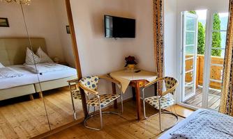 A cozy room with a large mirror, a small table, and two chairs. There is a television and access to the balcony with a view of the outdoors.