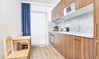A modern kitchen with wooden cabinets and a bright countertop. A small table with a chair is also present.