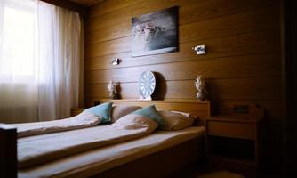 A cozy bedroom with a double bed and cool pillows. A picture and a wall clock hang on the wall, while light streams through a window.