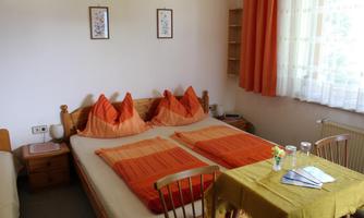 A cozy bedroom with a double bed and orange bedding. On the table are a flower vase and some drinks.