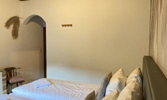 A simple room with two beds and neutral colors. A wooden ceiling and a chair complement the decor.