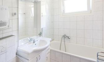 A modern bathroom with a bathtub and a sink. The walls are tiled, and the room feels bright and inviting.