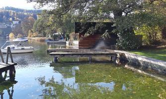 A quiet lake with a wooden dock and boats. Surrounded by trees and gentle hills in the background.