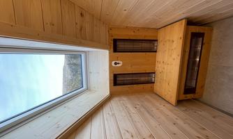 A cozy wooden room with a bench and large windows. Above the room is a skylight that lets in plenty of daylight.