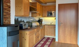 A cozy kitchen with wooden cabinets and modern amenities. In the background, mountain landscapes are depicted, creating a warm atmosphere.
