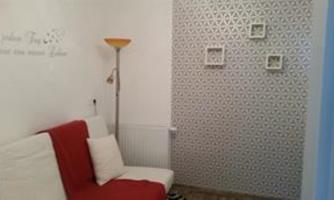 A small room with a white sofa and a red blanket. The wall is decorated with a modern pattern and has some picture frames.
