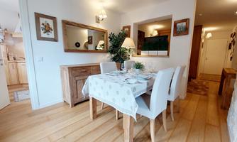 An inviting dining room with a wooden table and white chairs. Pictures hang on the wall, and a plant creates a pleasant atmosphere.