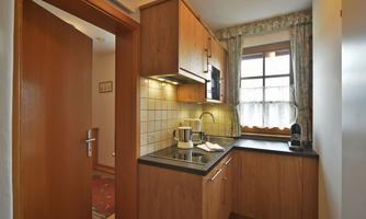 A small kitchen with wooden cabinets and modern equipment. A window provides natural light and coziness.