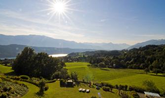 A picturesque landscape with green meadows and mountains in the background. The sun is shining brightly in the clear sky.
